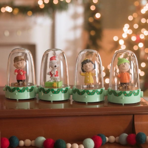 A set of Peanuts musical tapping figurines lined up on top of a piano, with a lit Christmas tree in the background.